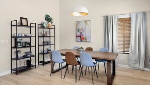A modern dining area with a wooden table, blue chairs, a black metal bookshelf, and a white pendant light. - Cozy and Stylish Home, Convenient Location, Putting Green and Grill  (Chandler)