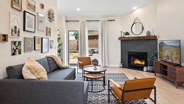 A modern living room with a fireplace, a ceiling fan, and a TV. - Cozy and Stylish Home, Convenient Location, Putting Green and Grill  (Chandler)