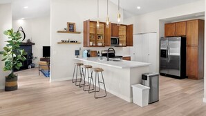 A modern kitchen with a central island, wooden cabinets, stainless steel appliances, and bar stools. - Cozy and Stylish Home, Convenient Location, Putting Green and Grill  (Chandler)