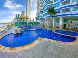 A hotel pool area with multiple swimming pools, lounge chairs, and a view of the city skyline.