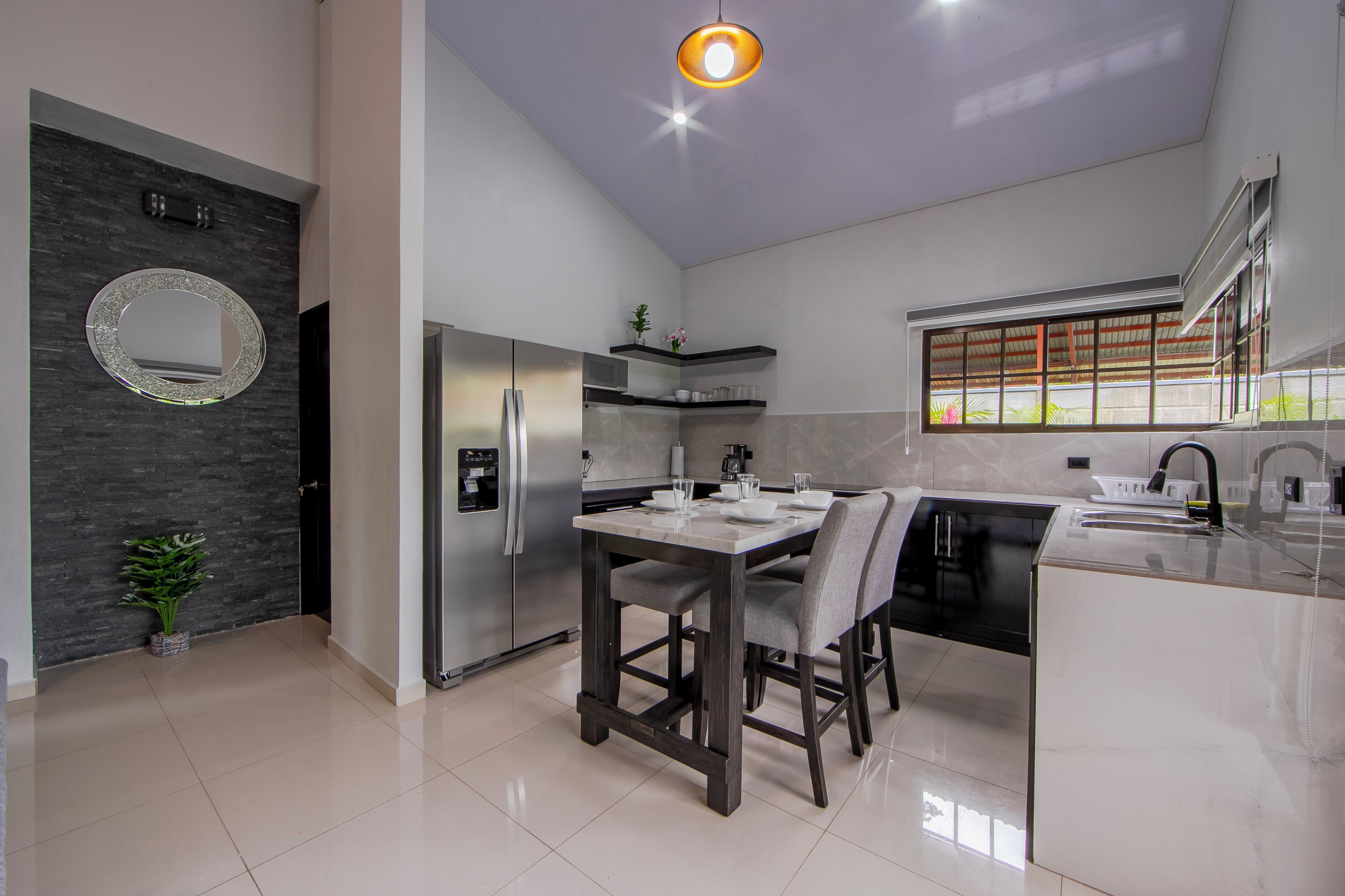A modern kitchen with a dining area, a refrigerator, a sink, and a window with a view.