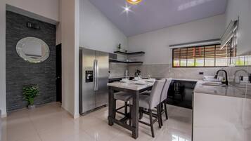 A modern kitchen with a dining area, a refrigerator, a sink, and a window with a view.