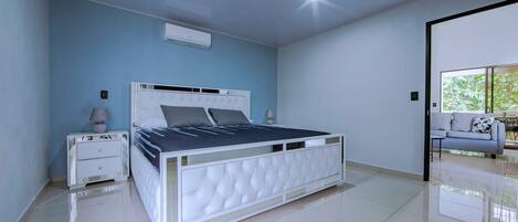A bedroom with a white bed, a nightstand, a lamp, and a sofa.