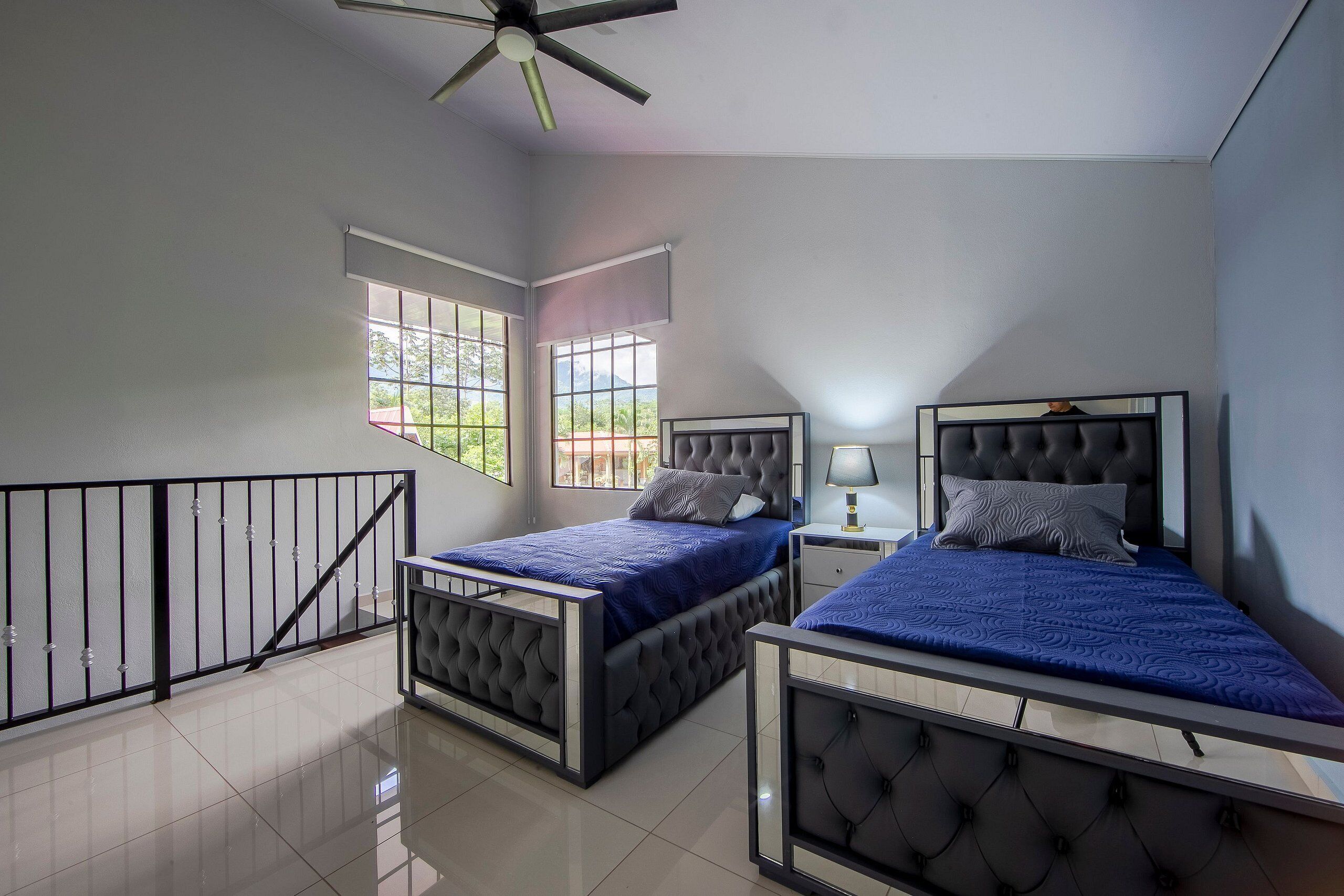 A bedroom with two beds, a ceiling fan, a window, and a nightstand.