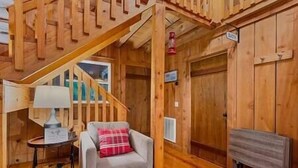 A wooden interior with a staircase, a chair with a plaid pillow, a lamp, and a fireplace. - Redbird Hideaway With Hot Tub (Edmonson County)