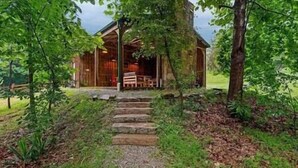 A rustic cabin with a stone staircase leading to a wooden porch. - Redbird Hideaway With Hot Tub (Edmonson County)