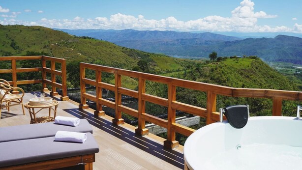 A wooden deck with a jacuzzi and lounge chairs overlooking a mountainous landscape.