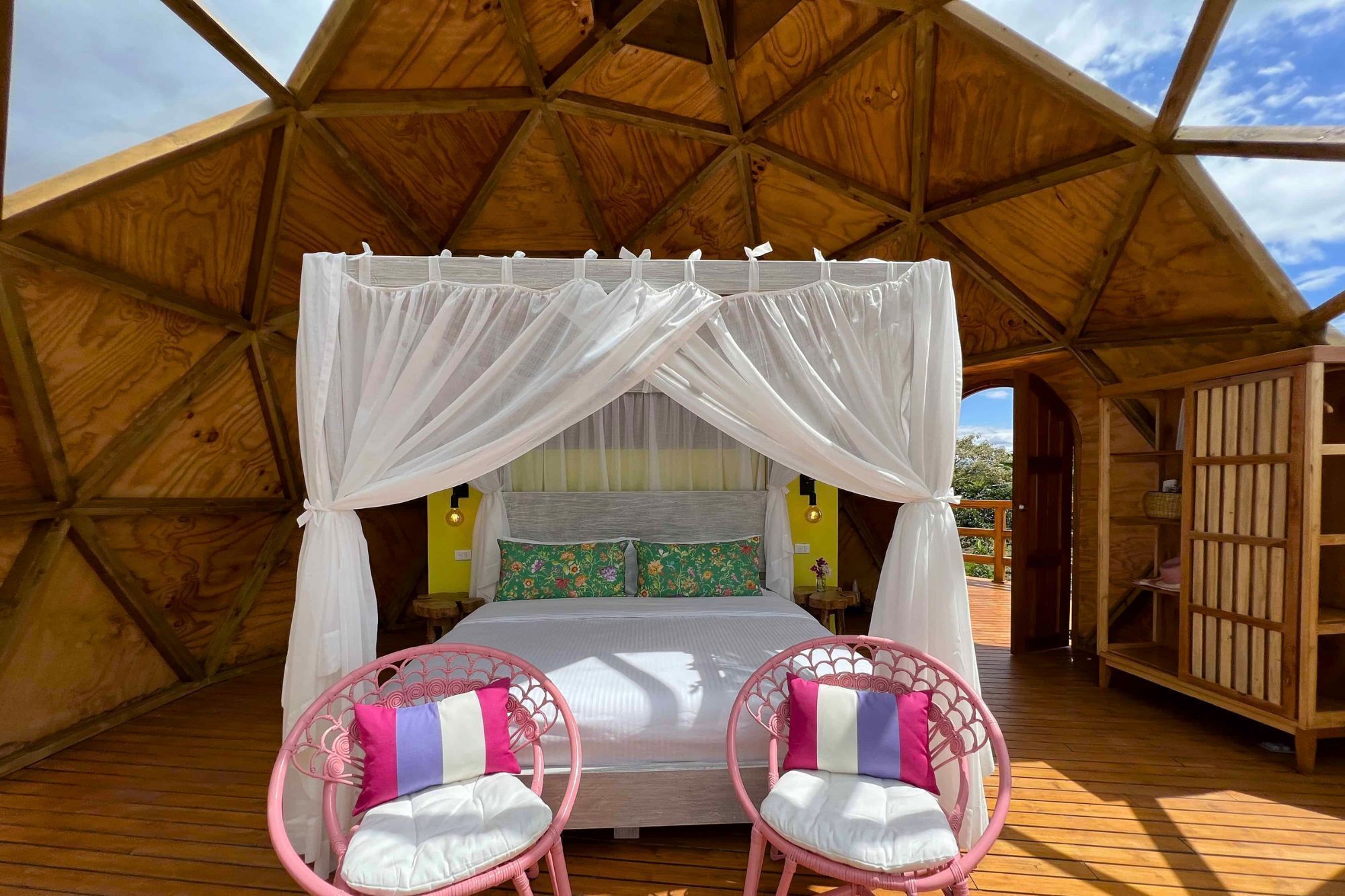 Una tienda de madera con una cama, dos sillas rosas y un dosel.