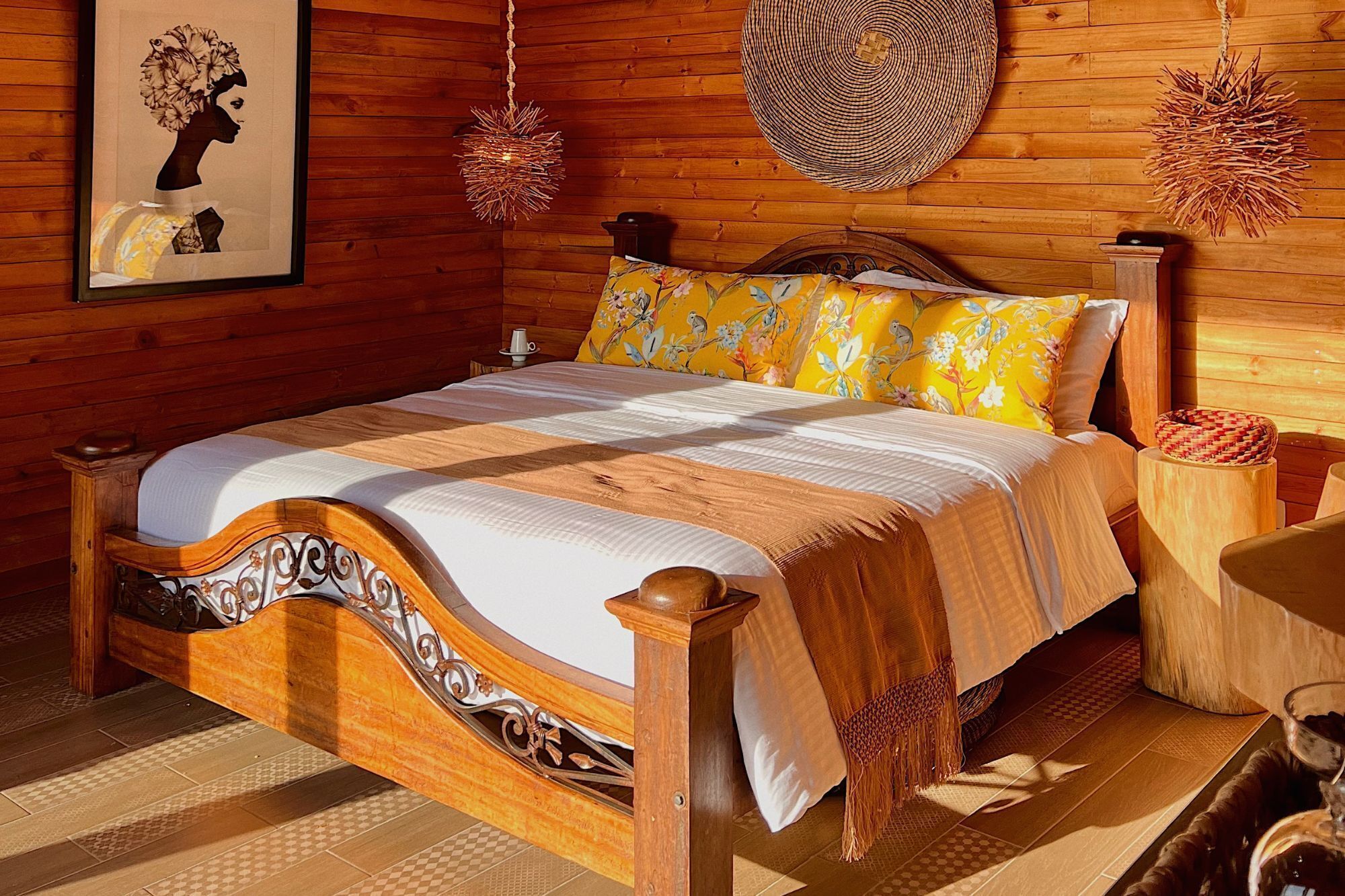 A wooden-framed bed with a floral-patterned bedspread and matching pillows, a woven wall hanging, and a woven basket on a wooden nightstand.