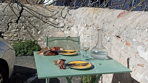 An outdoor dining area with a table and chairs, a vase, and a plate with cutlery. - Renovated fisherman's cottage  (Sète)