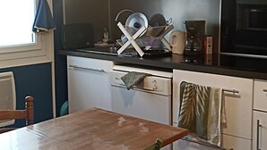 A kitchen with white cabinets, a wooden table, and a green folding chair. - Renovated fisherman's cottage  (Sète)