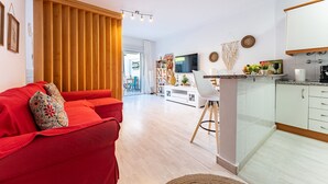 A modern living room with a red sofa, a wooden partition, and a kitchen with white cabinets and a TV. - MalagaSuite Yucas Fuengirola (Fuengirola)