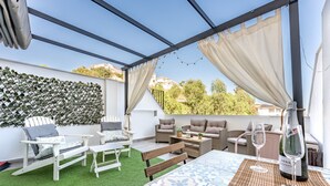 A covered outdoor seating area with wicker furniture, a table with a bottle of wine, and a view of the surrounding buildings. - MalagaSuite Yucas Fuengirola (Fuengirola)