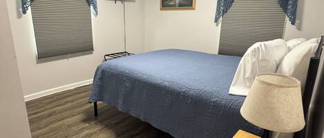Un dormitorio con cama, televisor, lámpara y un cuadro en la pared.