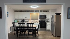 A modern kitchen with white cabinets, a stainless steel refrigerator, and a dining area with a table and chairs. - Charming 3-bedroom house with WiFi and AC in lovely Loretto (Loretto)