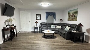 A living room with a sectional sofa, a coffee table, a TV mounted on the wall, a door, and a framed picture. - Charming 3-bedroom house with WiFi and AC in lovely Loretto (Loretto)
