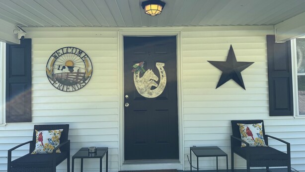 A porch with a sign reading "TRAILS END," a welcome sign, a horse's head decoration, and two chairs with floral cushions. - Charming 3-bedroom house with WiFi and AC in lovely Loretto (Loretto)