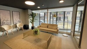 Un salon moderne comprenant un canapé, deux fauteuils, une table basse avec une plante, et de grandes fenêtres donnant sur la rue.