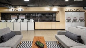 Un espace d’accueil avec un sol à carreaux, des canapés gris, une table basse en bois et un mur recouvert de carreaux.