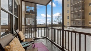 A balcony with a glass enclosure, seating area with patterned cushions, and a view of a cityscape. - Skyline Vistas | Downtown | Perfect Romantic Getaways (Atlanta)