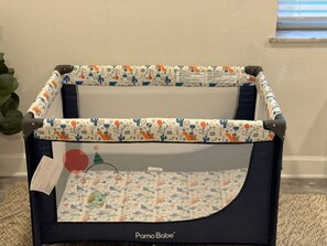 A Pamo Bobe playpen with a patterned fabric top and mesh sides, placed on a carpeted floor against a wall. - Terrace, Skyline View, Downtown, Restaurant & Bars (Atlanta)