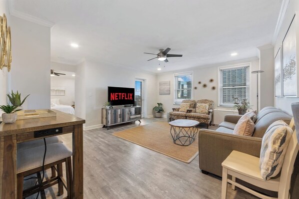 A modern living room with a wooden dining table, a sofa, a coffee table, and a TV displaying 'NETFLIX'. - Terrace, Skyline View, Downtown, Restaurant & Bars (Atlanta)