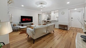 A modern living room with a flat-screen TV, a sofa, a coffee table, and a dining area with chairs.