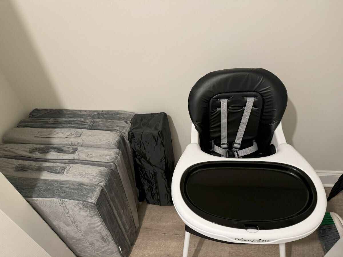 Une petite salle de bain avec des toilettes blanches et un abattant noir, un banc recouvert d’un tissu gris et un mur blanc.