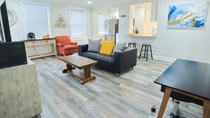 A modern living room with a sofa, coffee table, and a TV. There is a kitchen area with a refrigerator and a dining table. - 1BR Apt,Centrally located, City View (Atlanta)