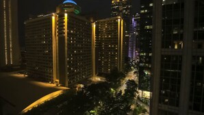 A nighttime view of a cityscape with high-rise buildings, including a hotel with multiple floors and balconies, and a distinctive blue-lit structure on top. - 1BR Apt,Centrally located, City View (Atlanta)