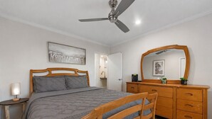 A bedroom with a bed, a wooden dresser, a mirror, a ceiling fan, and a nightstand.