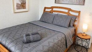 Una cama bien hecha con un edredón y almohadas de estampado geométrico, una lámpara de noche y un cuadro en la pared.