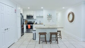 Una cocina moderna con armarios blancos, electrodomésticos de acero inoxidable y una isla central con taburetes.