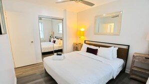 Une chambre d’hôtel avec un grand lit, un ventilateur de plafond, un miroir, une table de chevet avec une lampe et un plancher en bois.