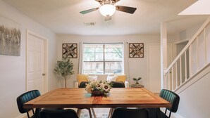 Comedor con mesa de madera, sillas negras, ventilador de techo y ventana con cortinas.