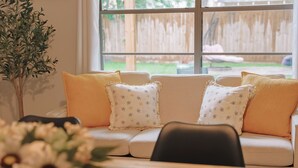 Una sala de estar acogedora con un sofá, cojines, una mesa y un jarrón de flores.