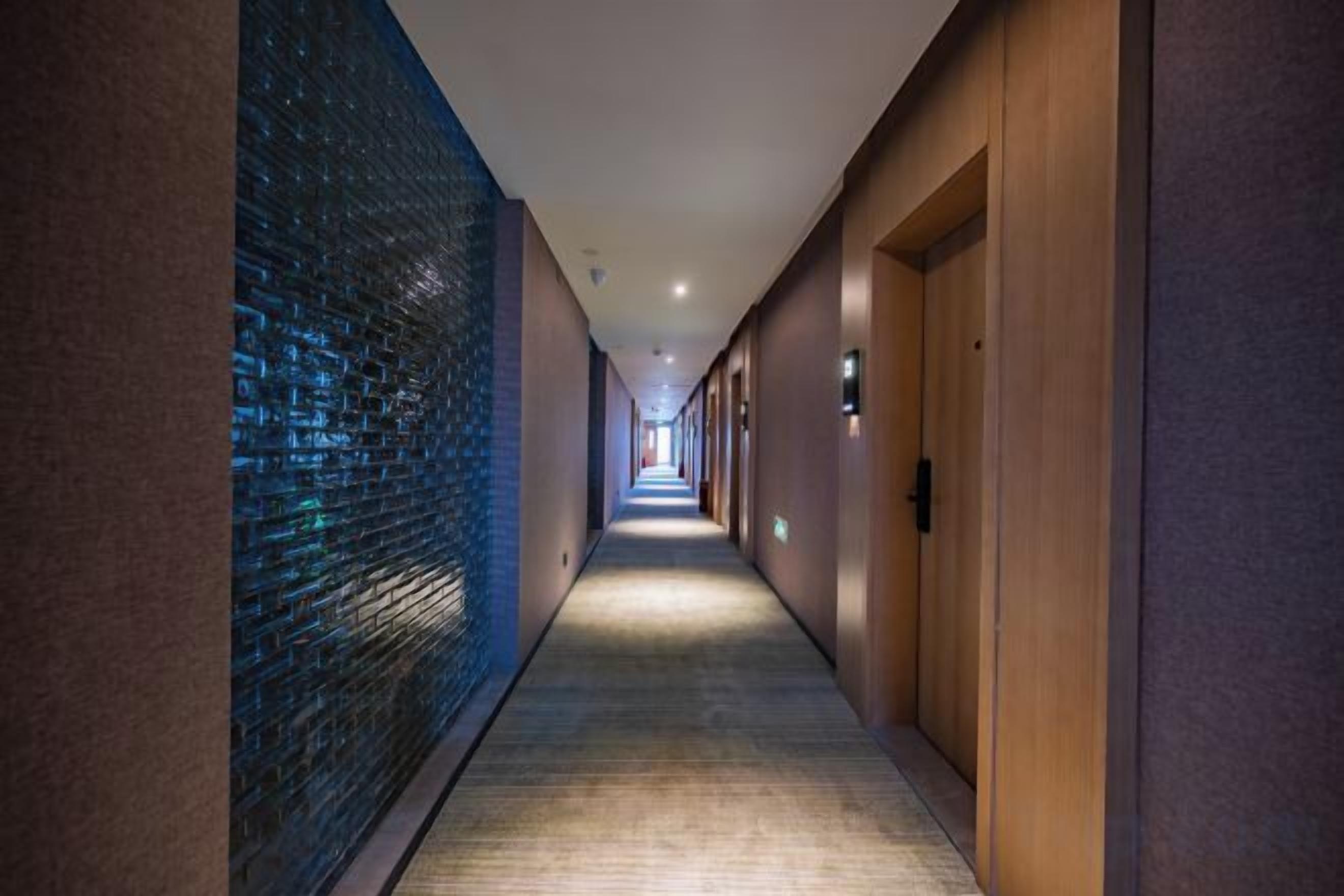 A corridor with a patterned wall on one side and a plain wall on the other, leading to a door at the end.