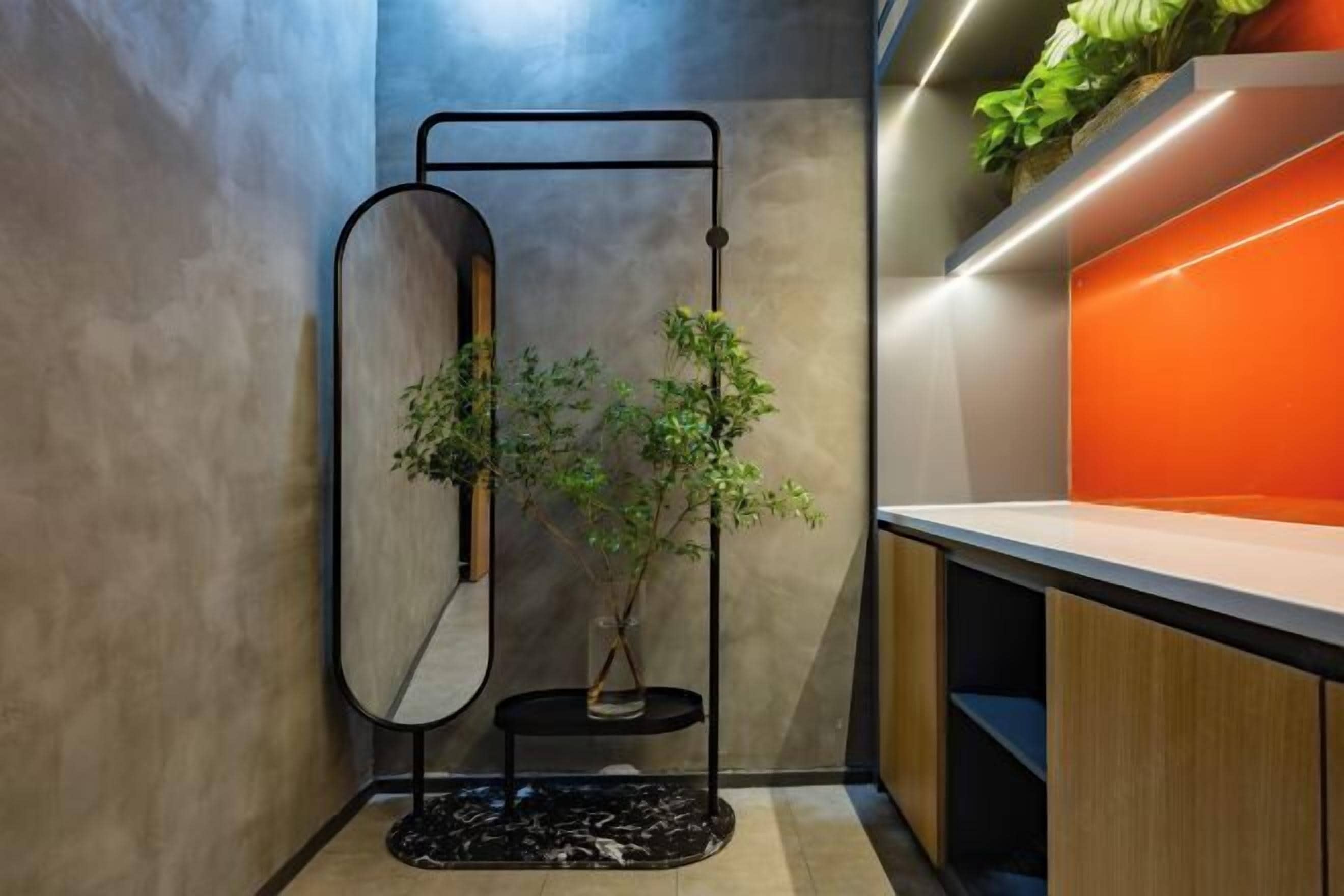 A modern bathroom with a wooden vanity, a black metal stand with a mirror, and a potted plant.