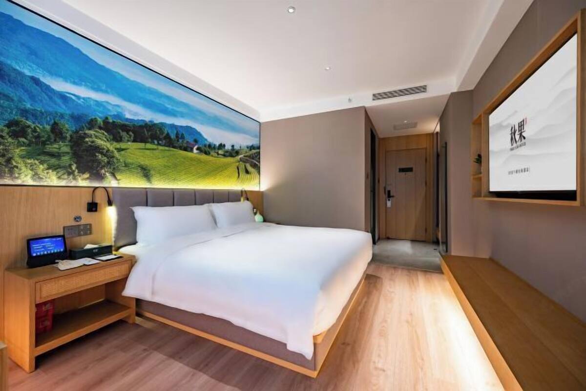 A modern hotel room with a large bed, a desk with a computer, and a large wall-mounted TV.