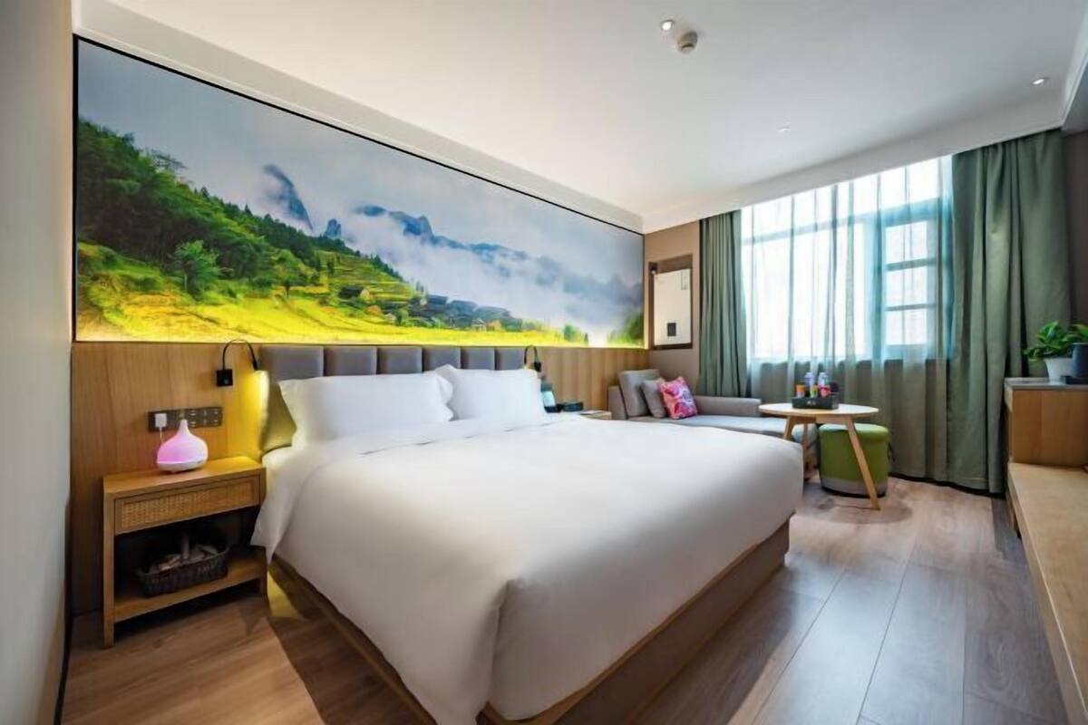 A hotel room with a large bed, a desk, a chair, a nightstand, and a wall-mounted TV.