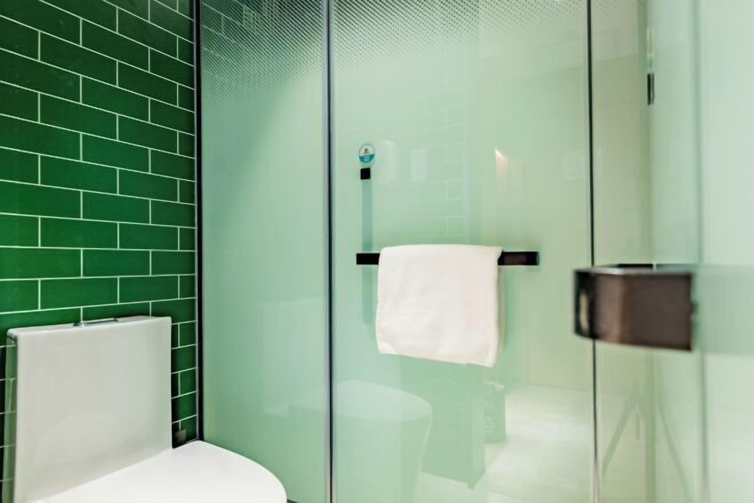 Un baño moderno con cabina de ducha de vidrio, inodoro blanco y pared revestida de azulejos verdes.