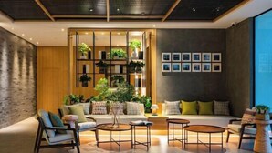 Una sala de estar moderna con un sofá, sillones y mesas de centro. Hay plantas en estanterías y una ventana grande con cuadros en la pared.
