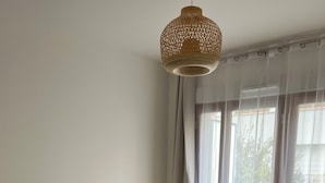 Un dormitorio con una cama grande, una lámpara colgante, cortinas translúcidas y vistas al exterior.