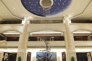 Vestíbulo de hotel con techo alto, iluminación decorativa y una columna central.