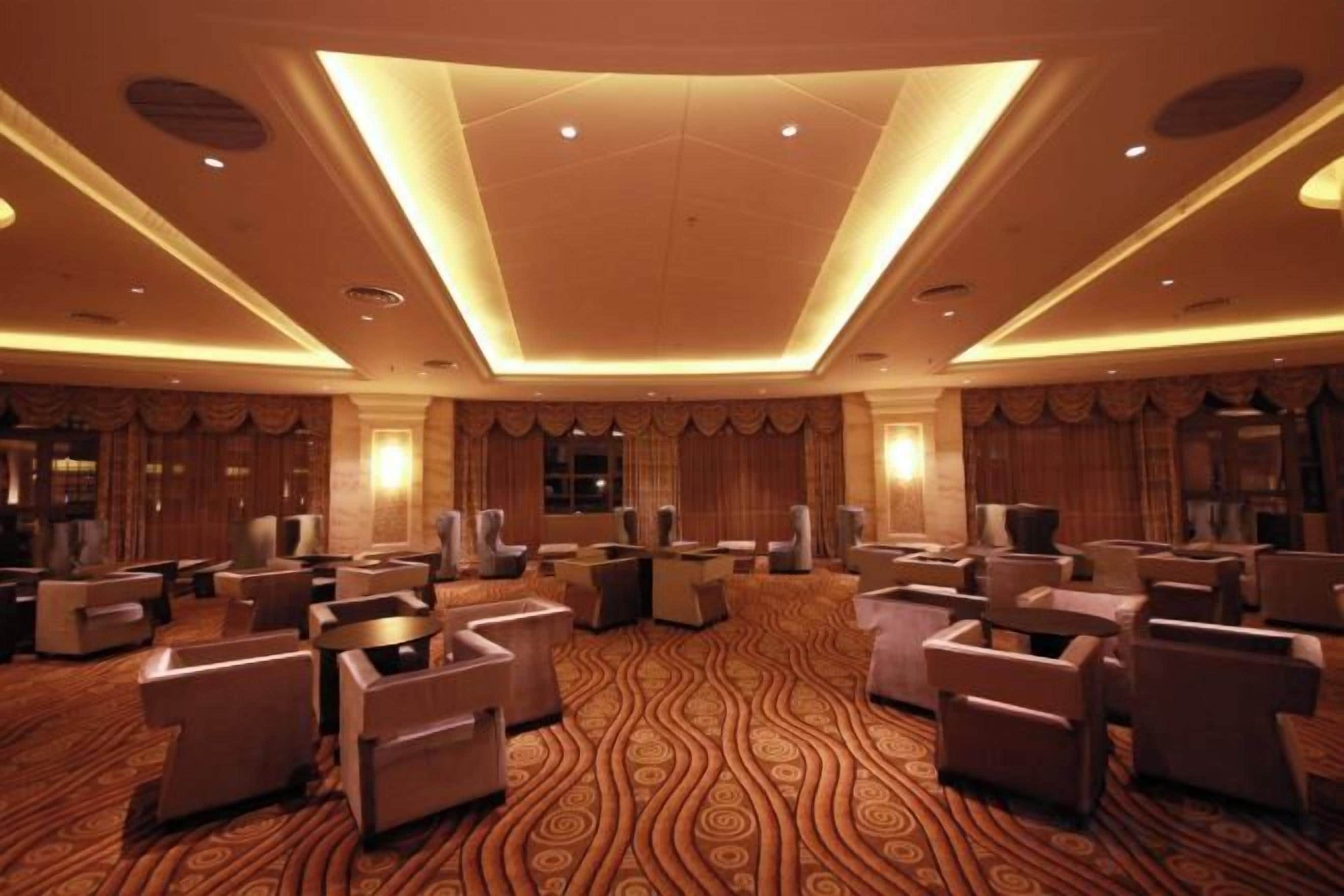Un hall d’hôtel doté d’un tapis à motifs, de plusieurs espaces aménagés pour s’asseoir et d’un plafond haut avec des luminaires encastrés.
