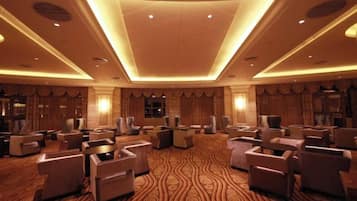 Un hall d’hôtel doté d’un tapis à motifs, de plusieurs espaces aménagés pour s’asseoir et d’un plafond haut avec des luminaires encastrés.