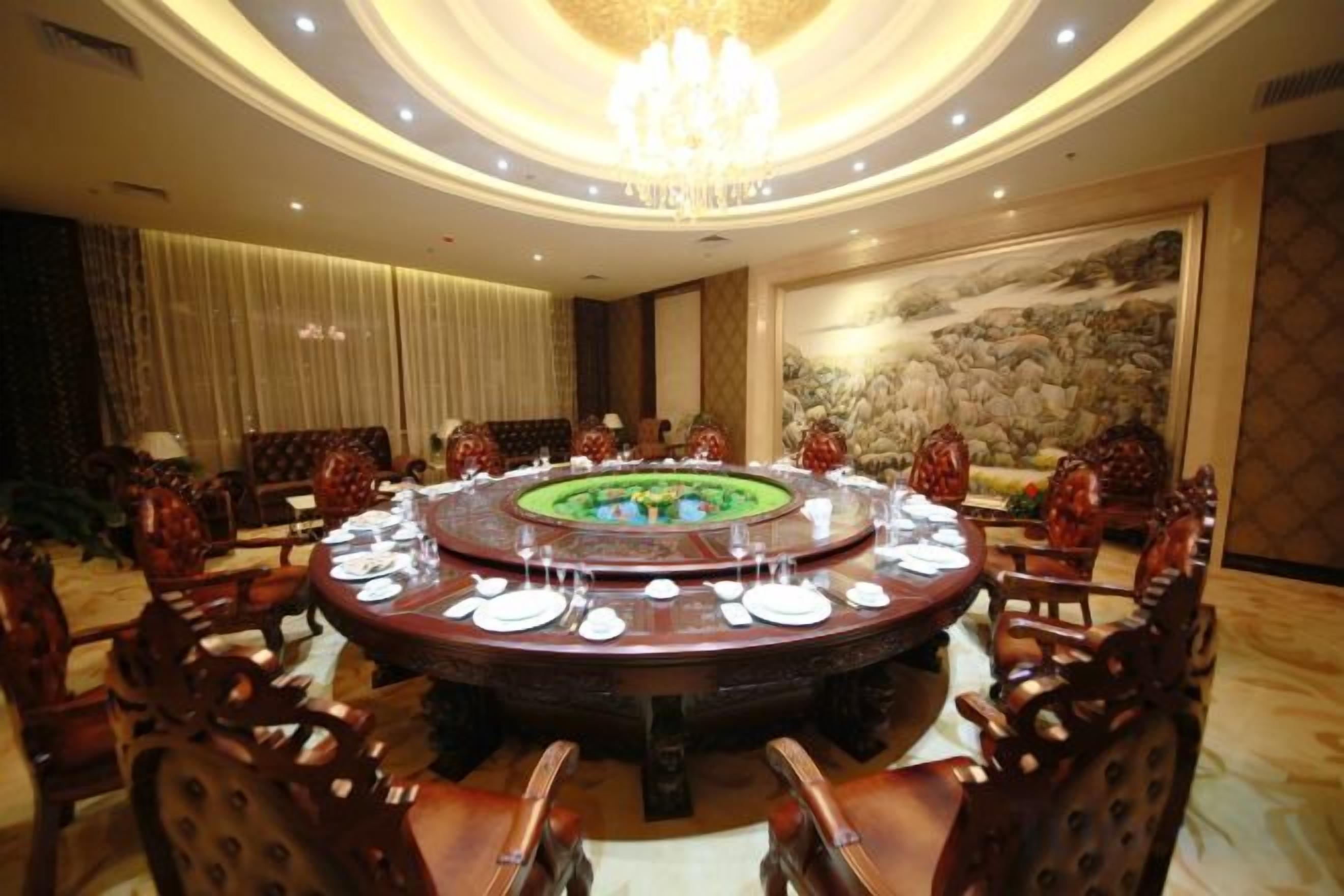 A round dining table with chairs, a chandelier, and a painting on the wall.