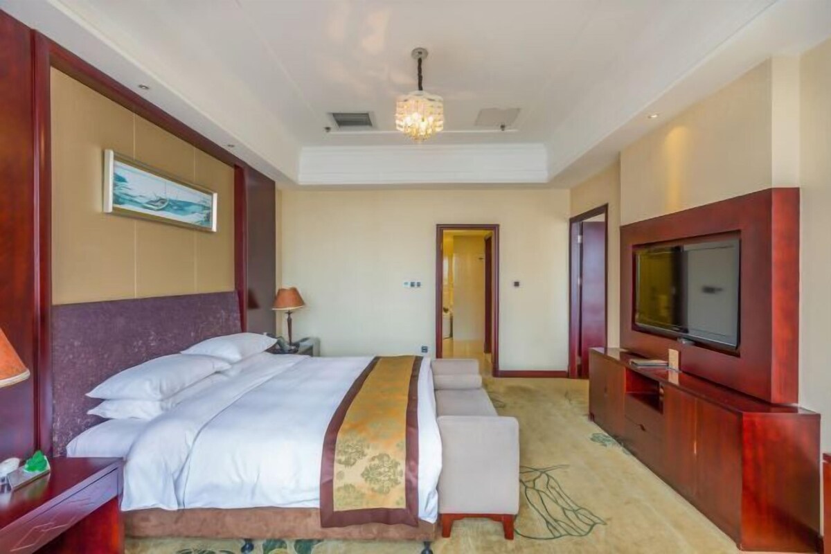 A hotel room with a large bed, a TV, a desk, and a chair.