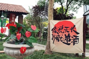 Un jardín con una jardinera con forma de corazón, un estandarte rojo con caracteres japoneses y un edificio con techo de tejas.