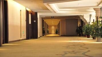 Pasillo de hotel con puertas a ambos lados, piso alfombrado y plantas en macetas a lo largo de la pared derecha.